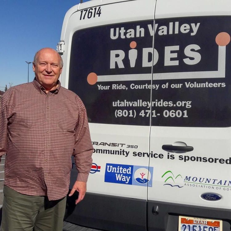 Volunteer man stands next to the exterior of a passenger van.