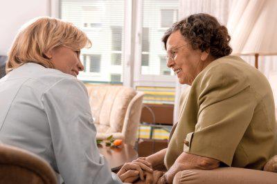 Two women are sitting across from each other on chairs, smiling at each other.