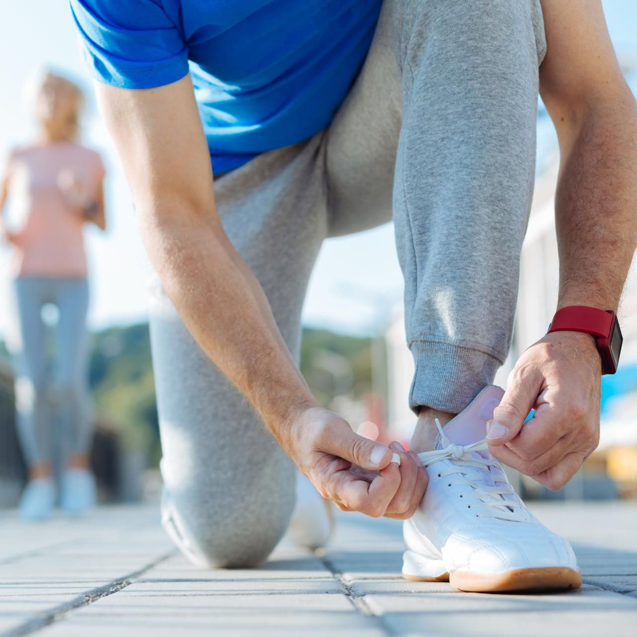 Man in athletic pants is kneeling on one knee while tying his shoes.